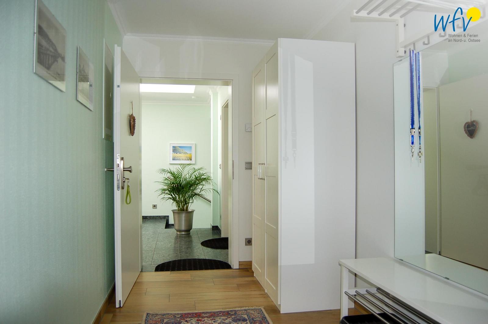 Flur mit Holzboden, Spiegelschrank und Pflanze im Hintergrund.