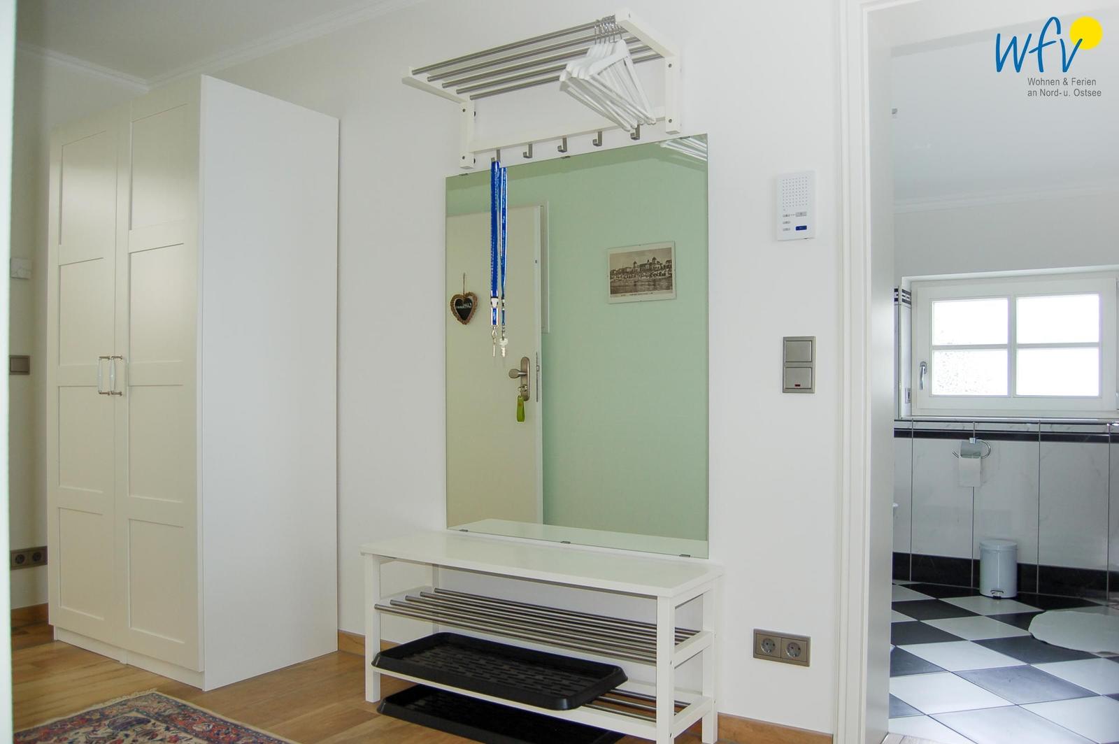 Eingangsbereich mit Spiegelschrank, Kleiderständer und Garderobe. Blick in die Badewanne mit Fliesenboden.
