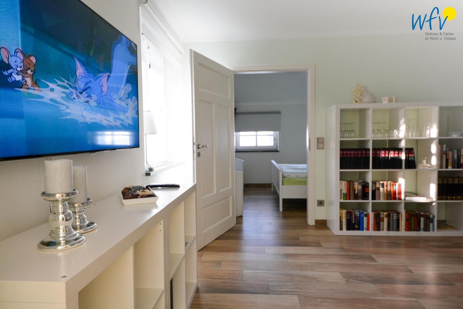 Wohnzimmer mit TV, Bücherregal und Blick in Schlafzimmer mit Bett.
