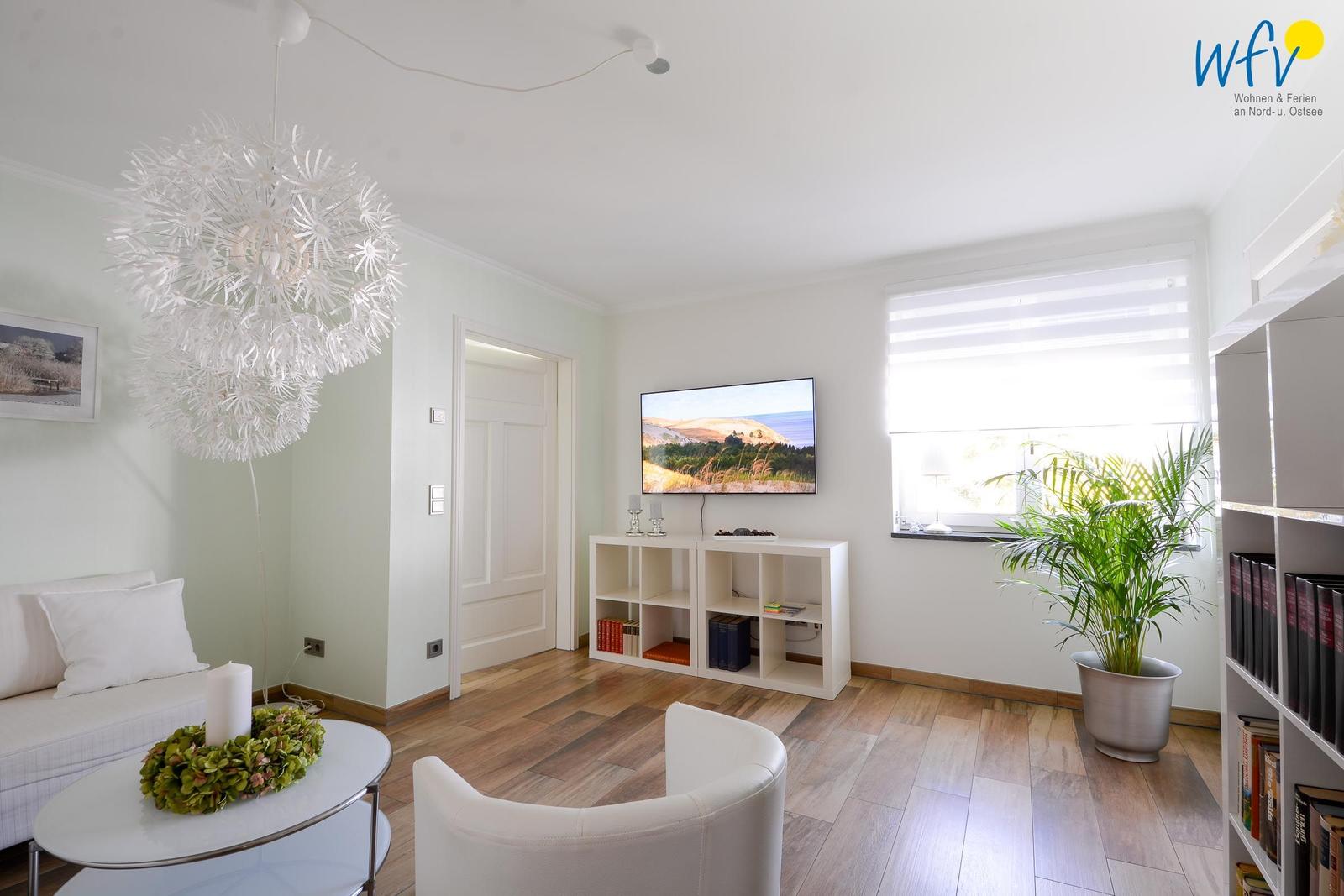 Wohnzimmer mit TV, Sofa, Stuhl und Pflanze. Holzboden und weißer Schrank.