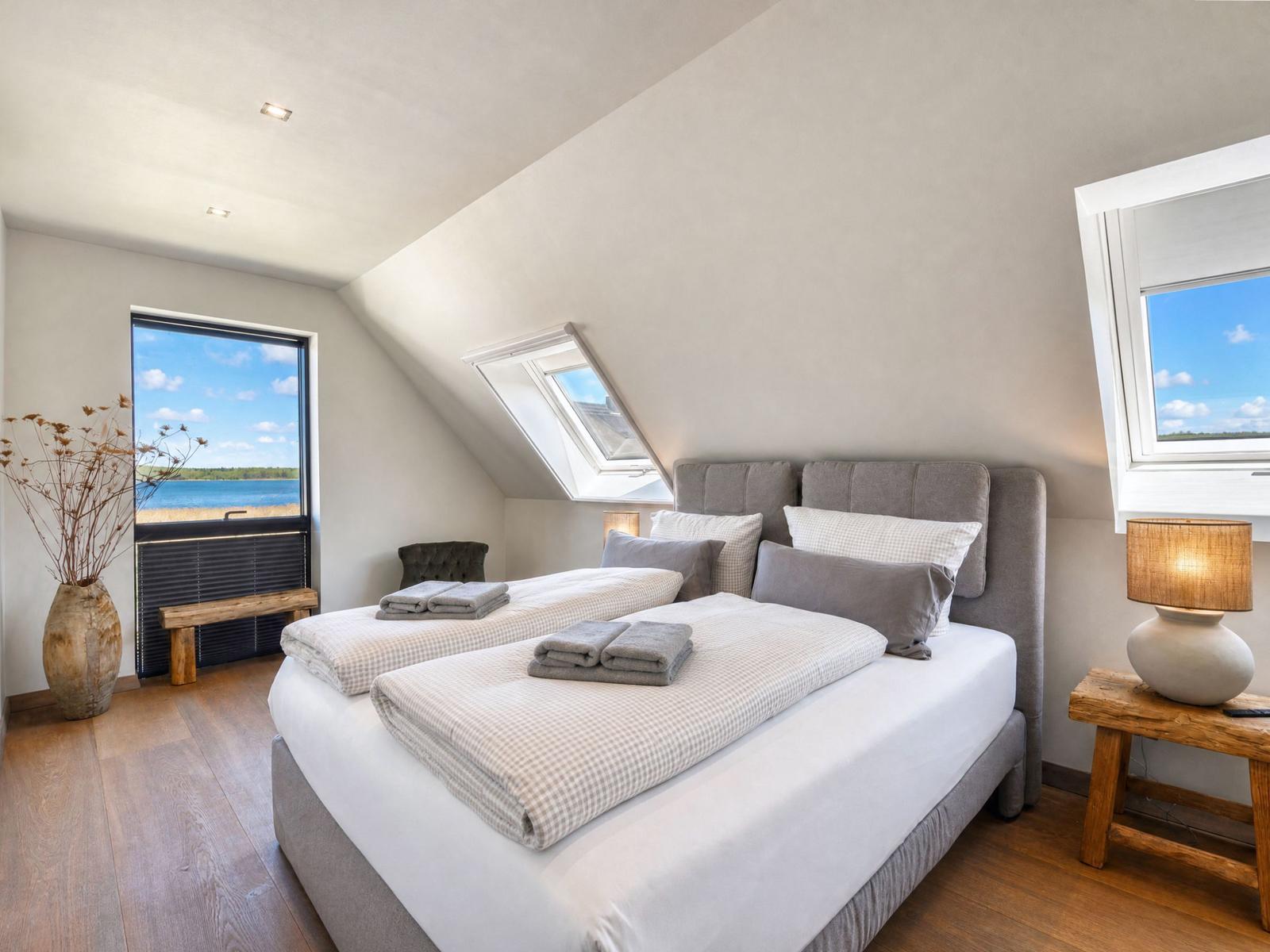 Bedroom with double bed, windows, and skylight. Wooden floor and rustic furniture.