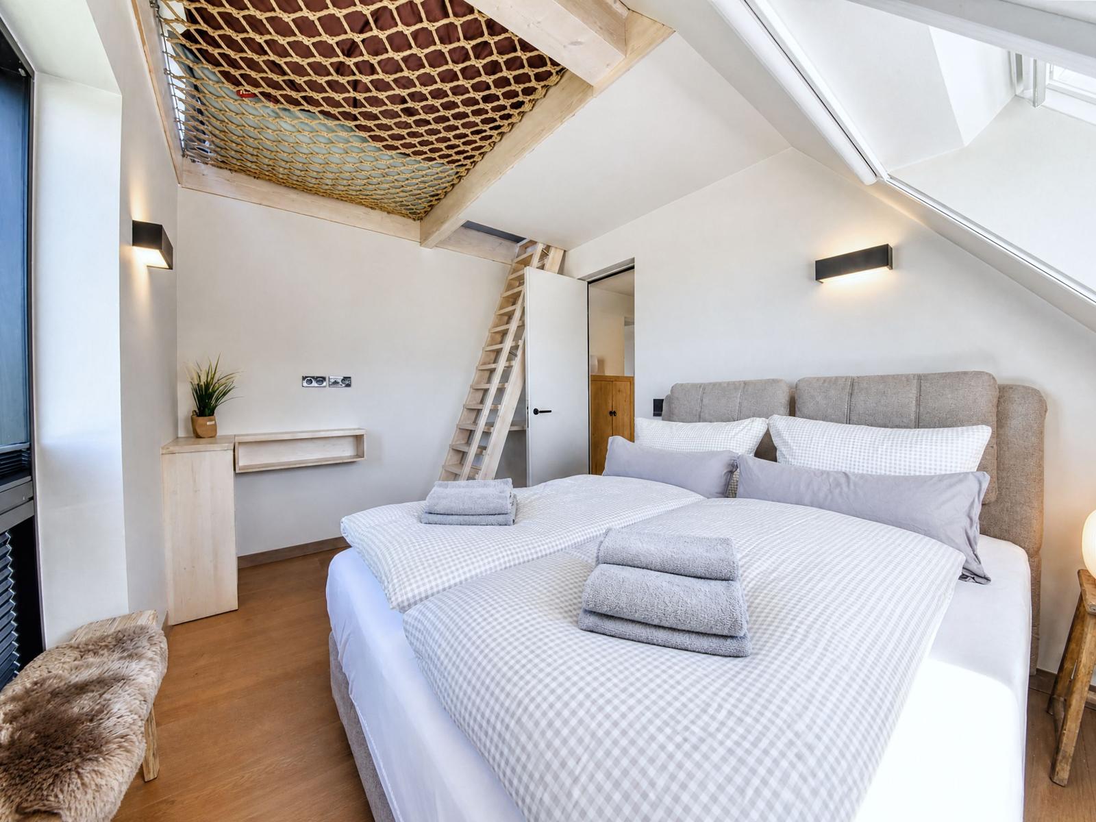 Bedroom with double bed, wooden floor, and climbing net under sloped ceilings.