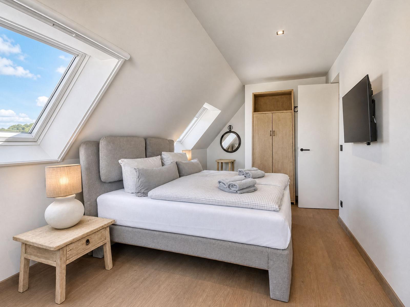 Bedroom with skylight, bed, wardrobe, and wall-mounted TV.