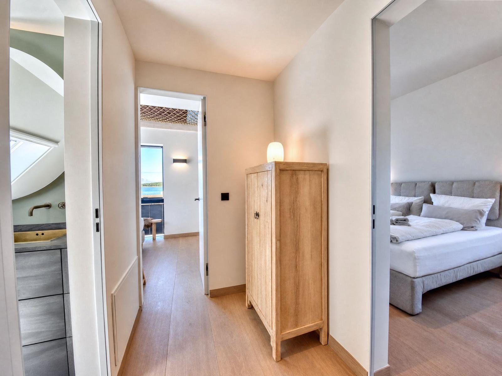 Bedroom with bed and wardrobe. Corridor to bathroom and terrace with sea view.