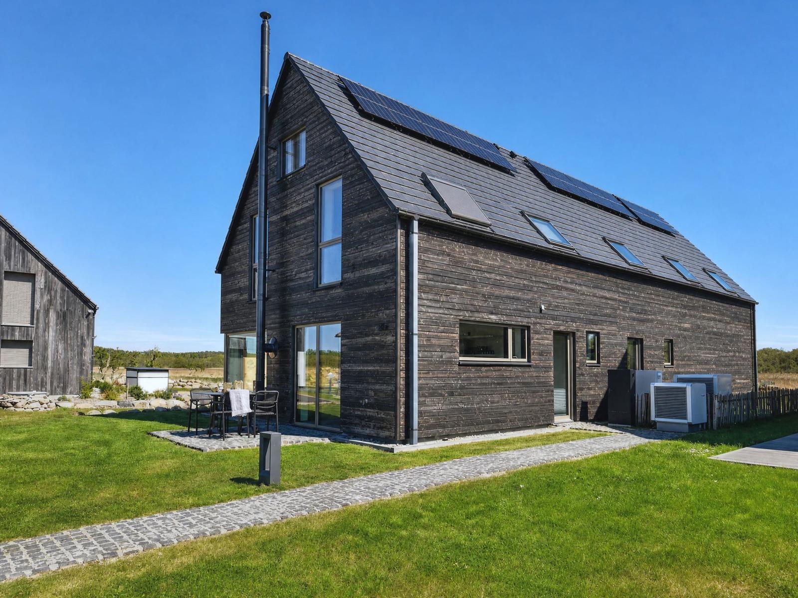 Modern wooden house with solar panels and garden. Terrace with table and chairs.
