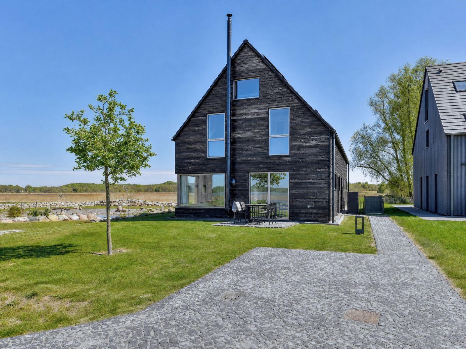 Wooden house with large garden and terrace. Cobblestone path leads to the entrance.