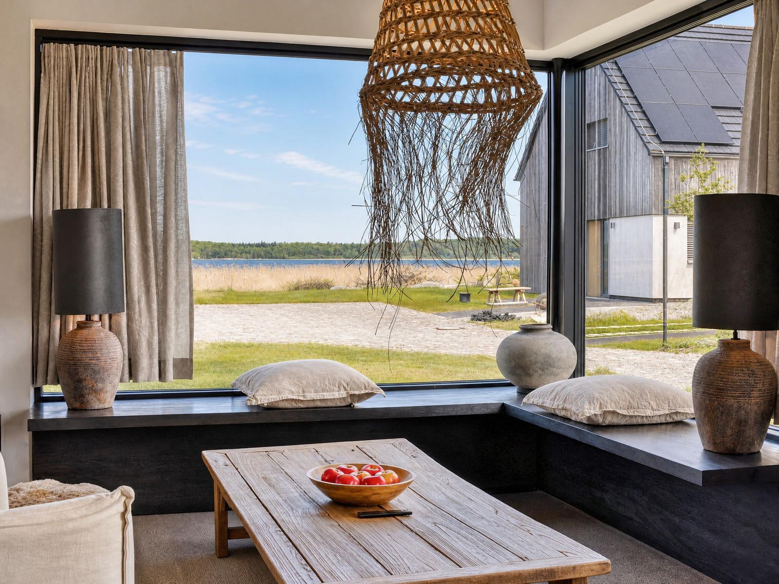 A room with large windows, a seating bench, table, and view of lake and forest.