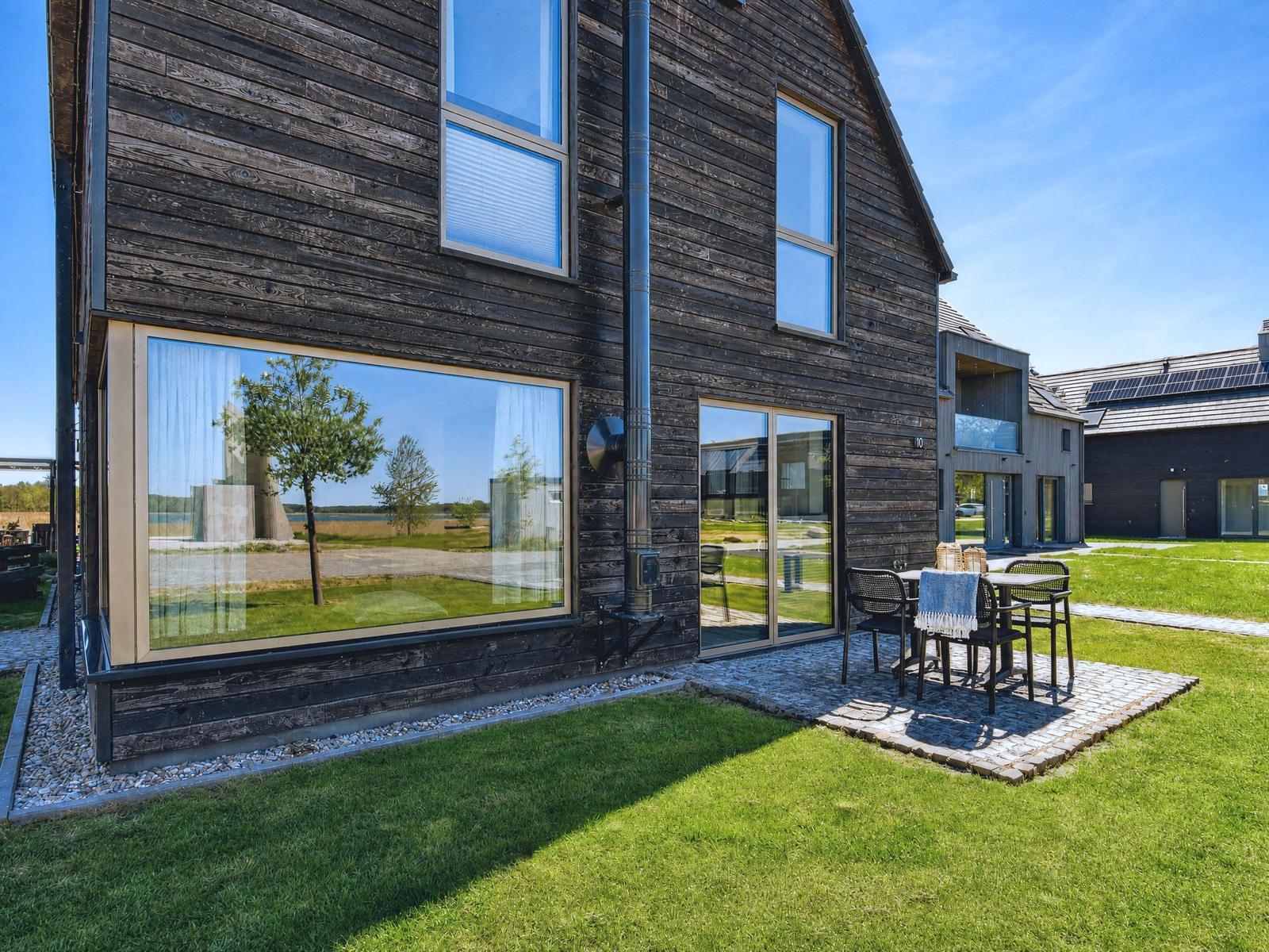 Modern wooden house with large window and terrace with table and chairs.