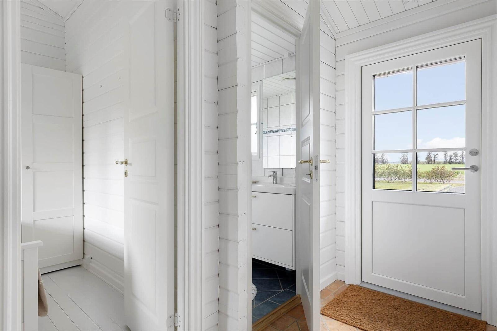 Entrance with white door and garden view. Adjacent room with sink and mirror.