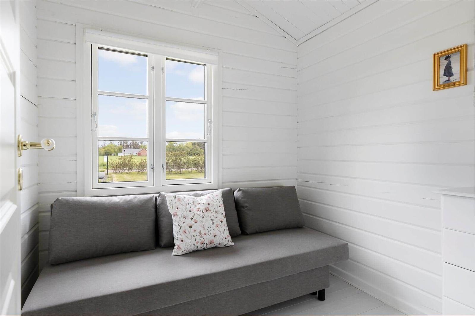 A gray seating area with cushions under a window in a white wooden house.