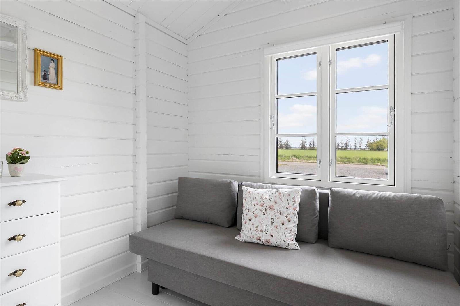 A room with gray sofa, white dresser, and window view of field.