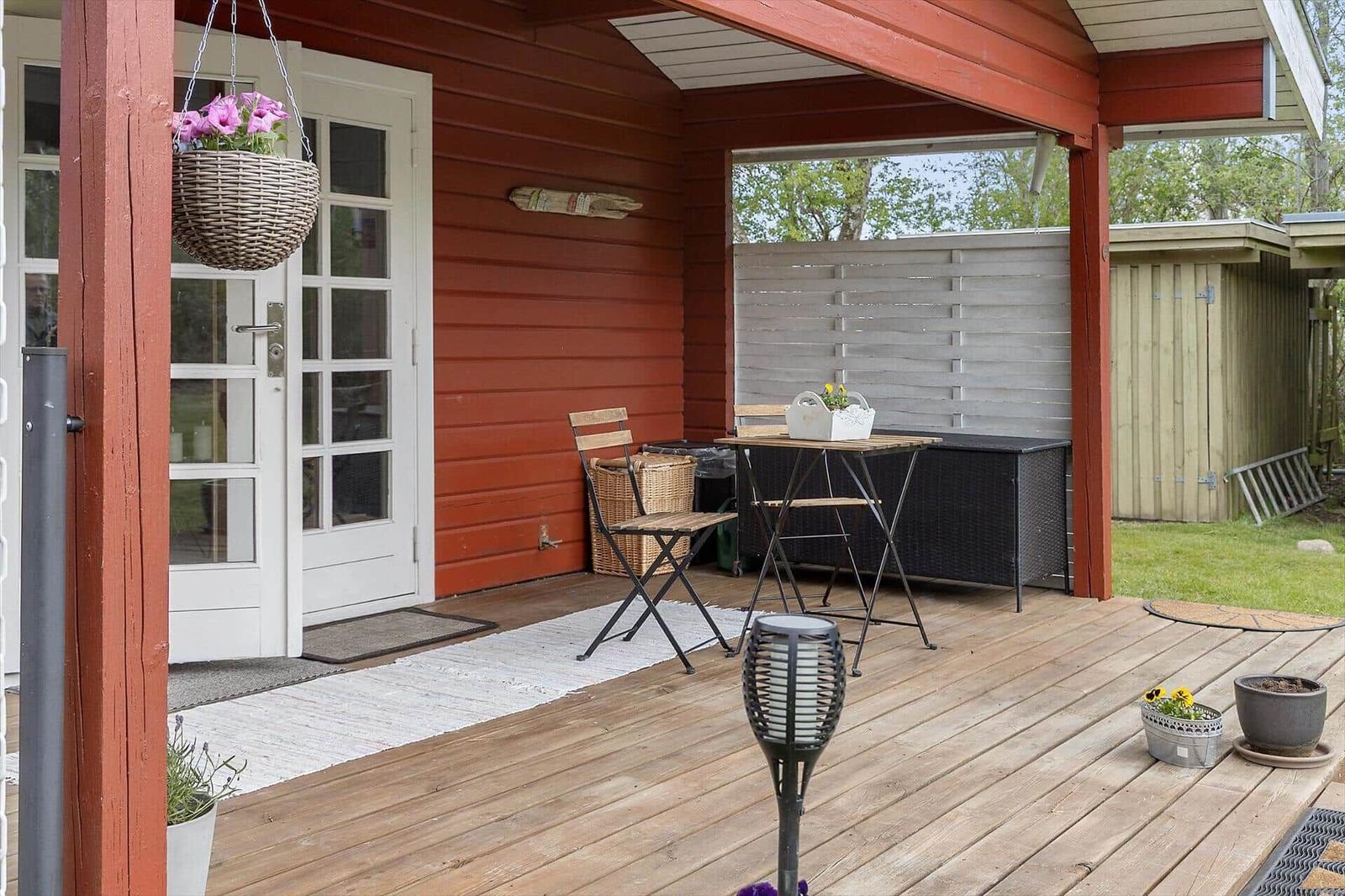 Deck with table, chairs, and flower baskets at red house with white doors.