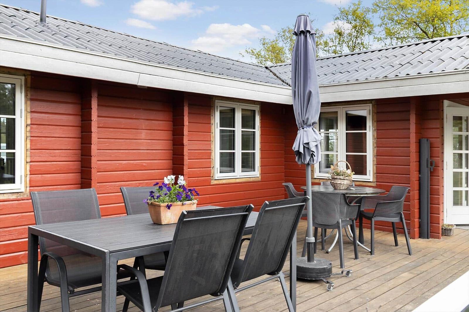 Red wooden exterior with terrace, table, chairs, and umbrella.