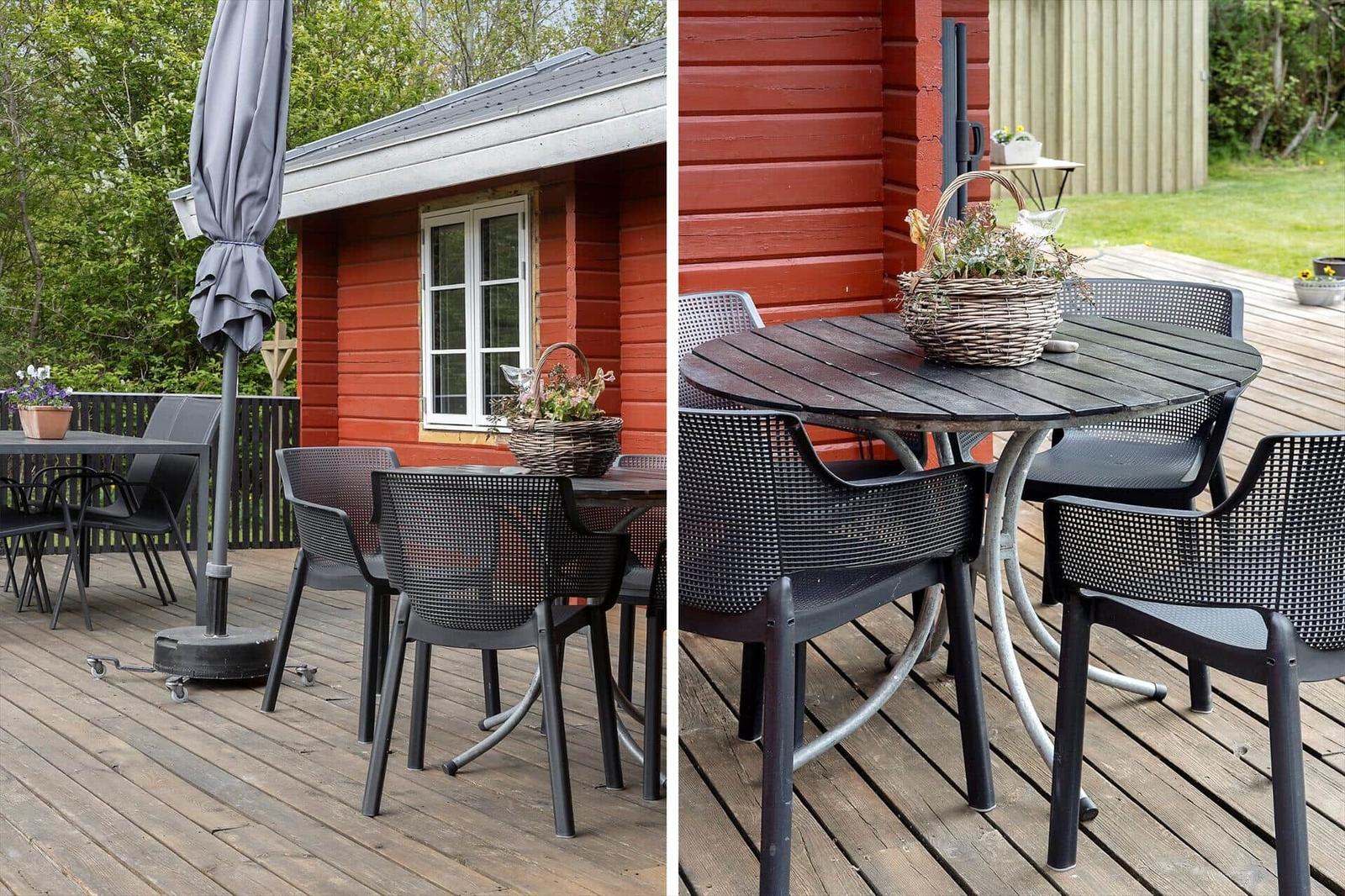 Red wooden cabin with terrace, table, and chairs. Flower basket on table.