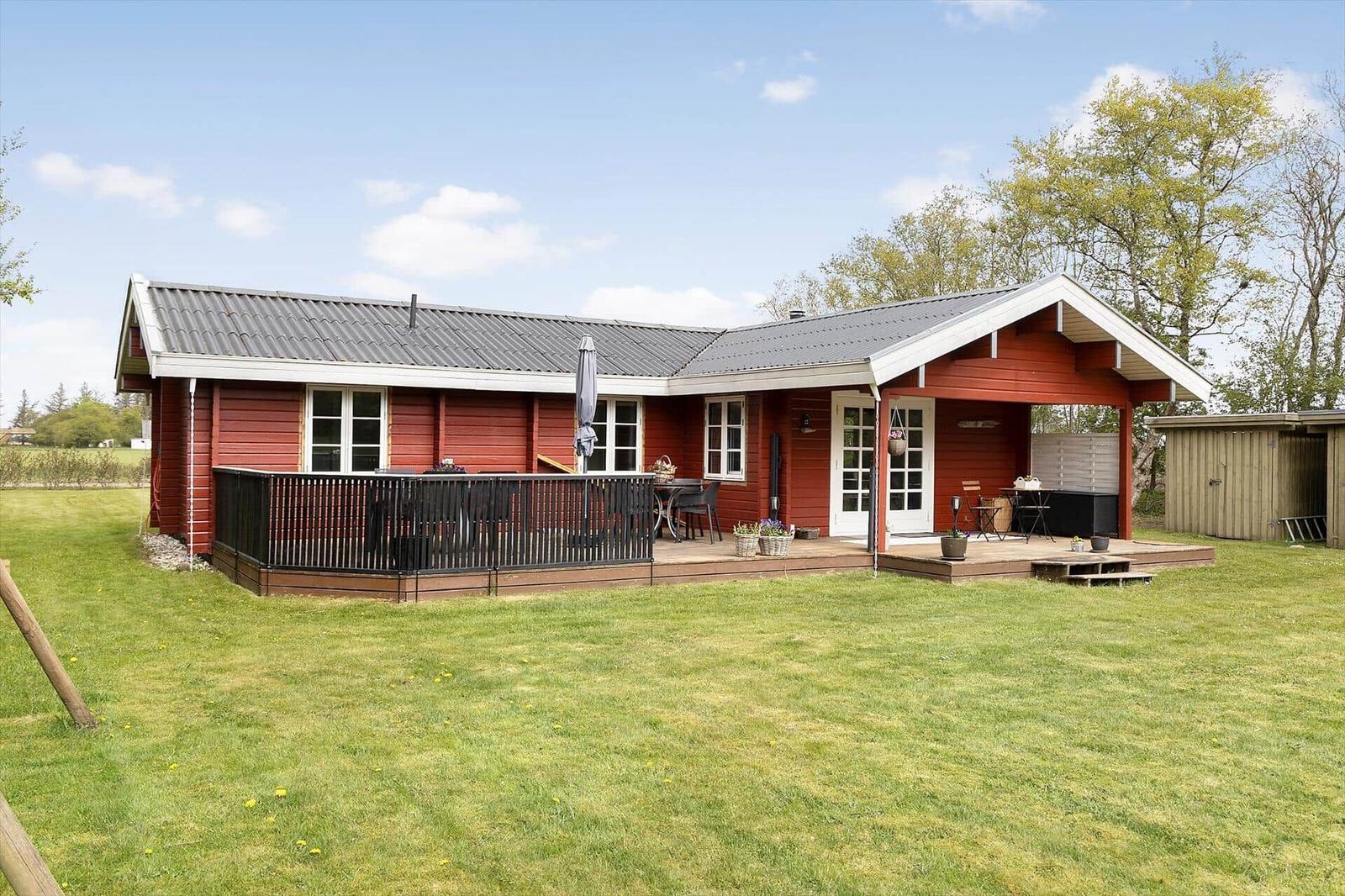 Red wooden house with terrace and garden. Outdoor table, chairs, and grill are available.