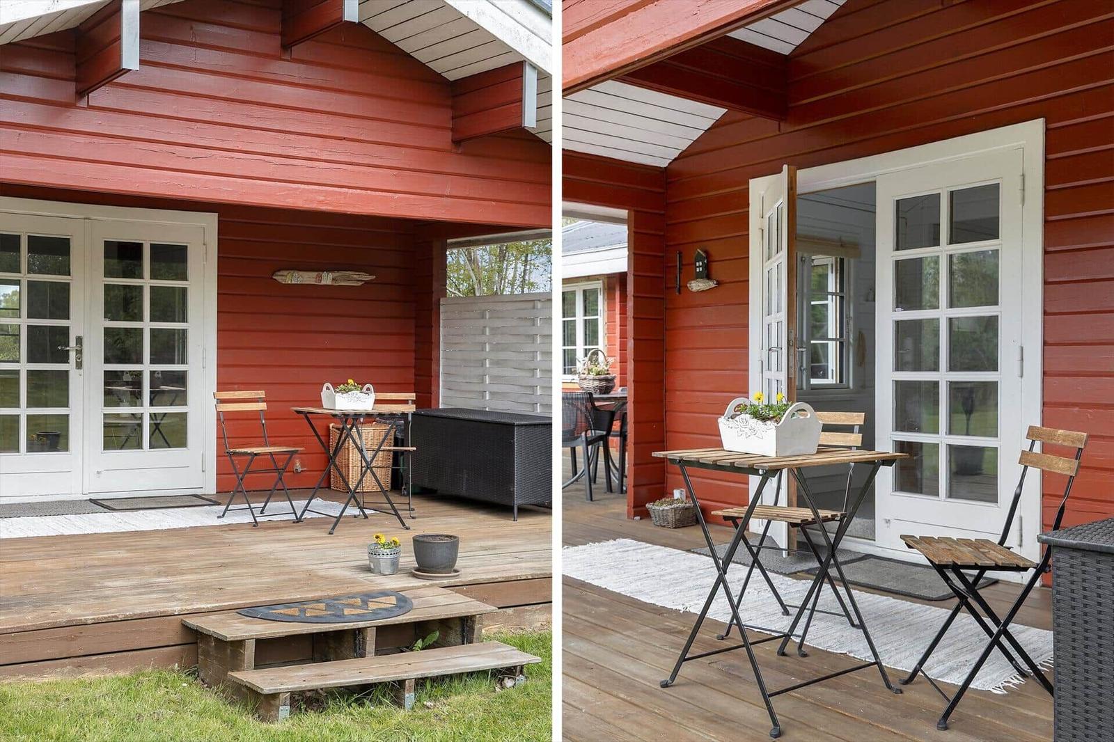 Red wooden house with terrace, table, and chairs. Door leads into the house.
