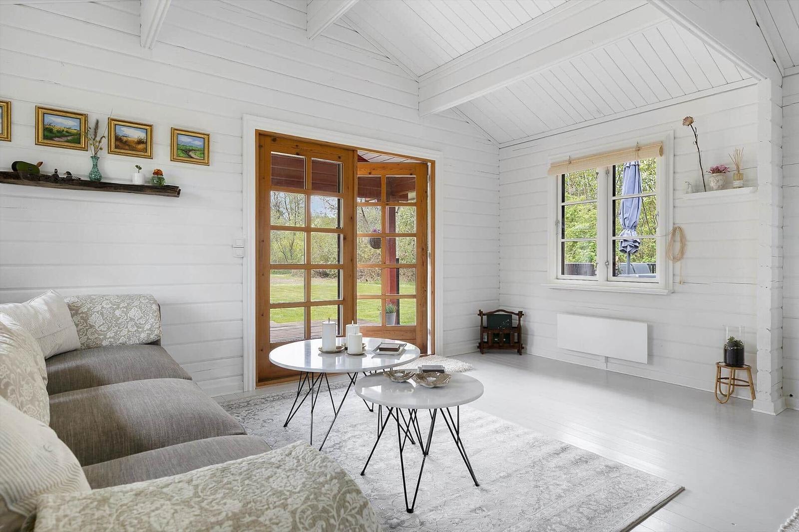 Living room with sofa, tables, and windows. Wooden door leads outside.
