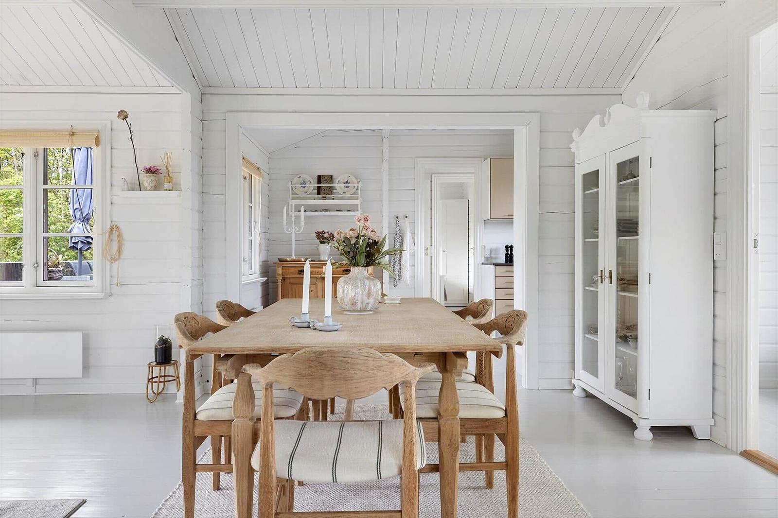 Dining room with wooden table, chairs, and white sideboard. Windows and ceiling are white.