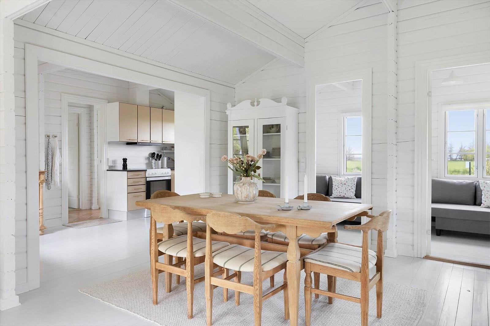 Dining area with wooden table and chairs, kitchen and living area in the background.