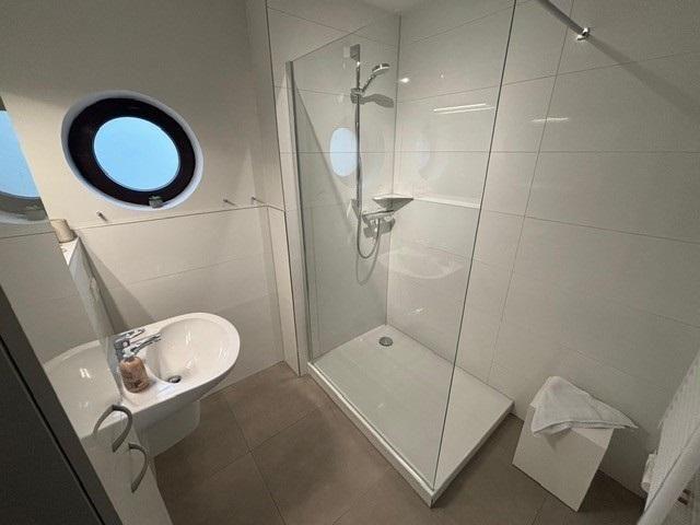 Badezimmer mit Dusche, Toilette und runden Fenster.