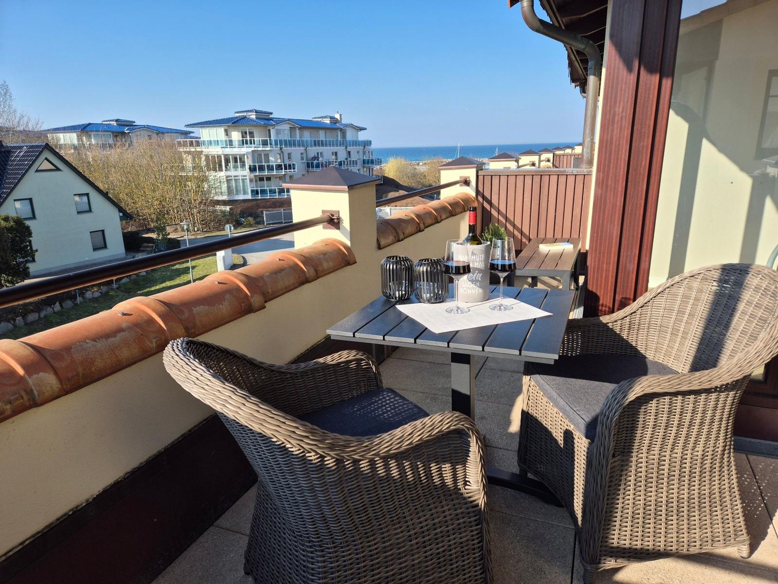 Terrasse mit Tisch und Stühlen, Blick auf Meer und Gebäude.