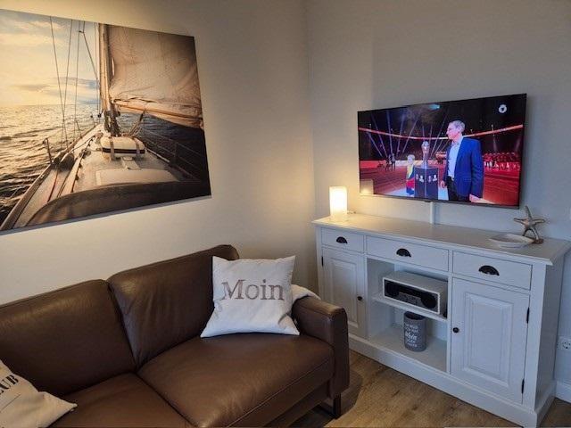 Ein Wohnzimmer mit Sofa, Fernseher und Wandbild eines Segelboots.