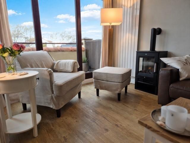 Ein Wohnzimmer mit Sitzgelegenheiten, einem Kaminofen und Blick auf Balkon.