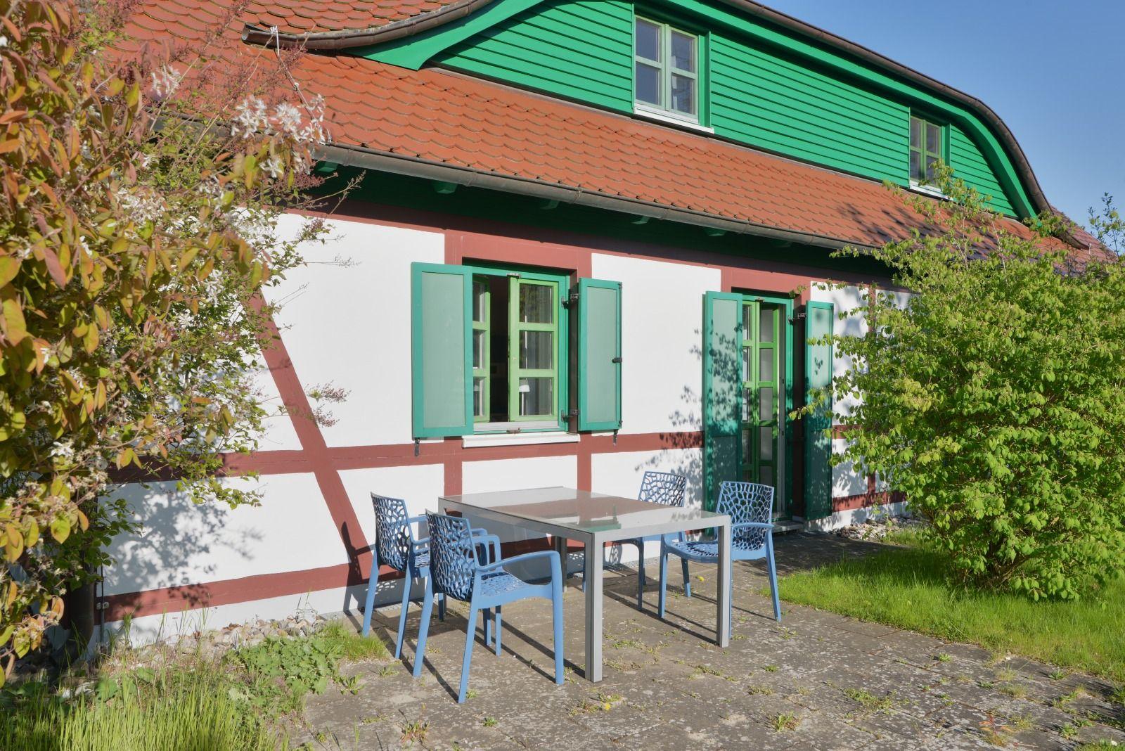 Haus mit grünen Fenstern und Terrasse mit Tisch und Stühlen.