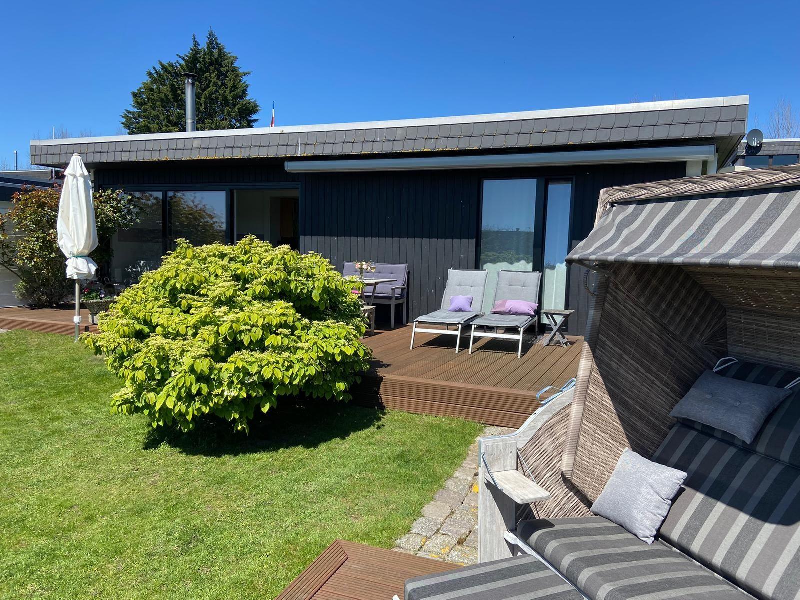 Terrasse mit Liegestühlen und Sonnenschutz, Grünfläche und modernes Haus im Hintergrund.