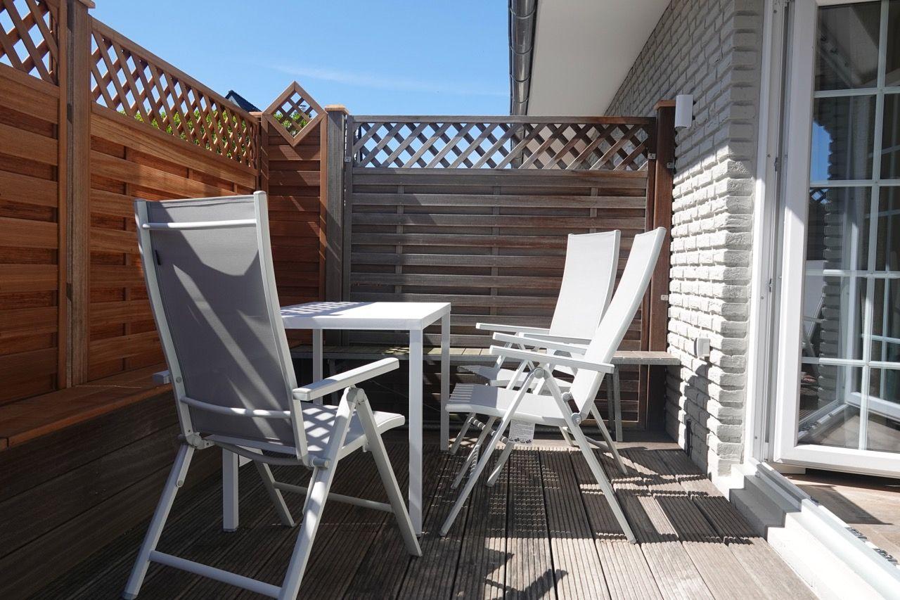 Terrasse mit Tisch und Stühlen, umgeben von Holzgeländern und Backsteinwand.