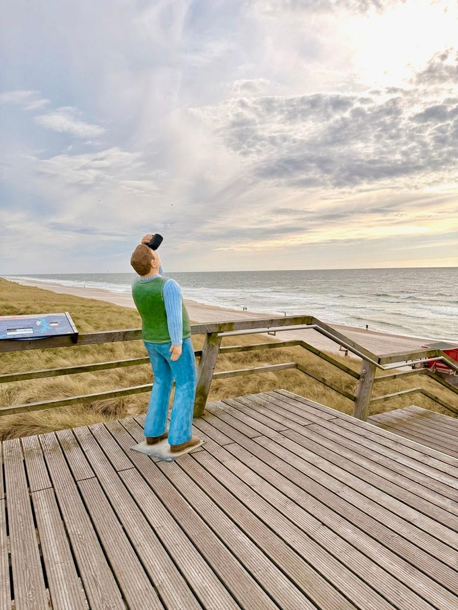 Statue eines Mannes mit Fernglas auf Holzterrasse am Strand