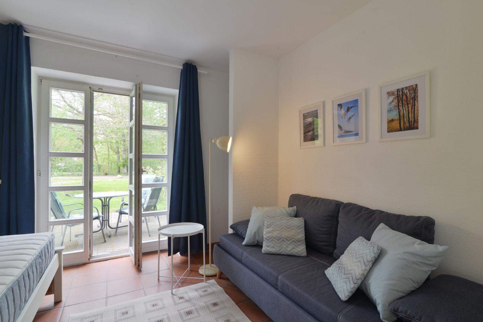 Ein Wohnzimmer mit Sofa, Bildern und Terrassentür. Blick auf Garten.