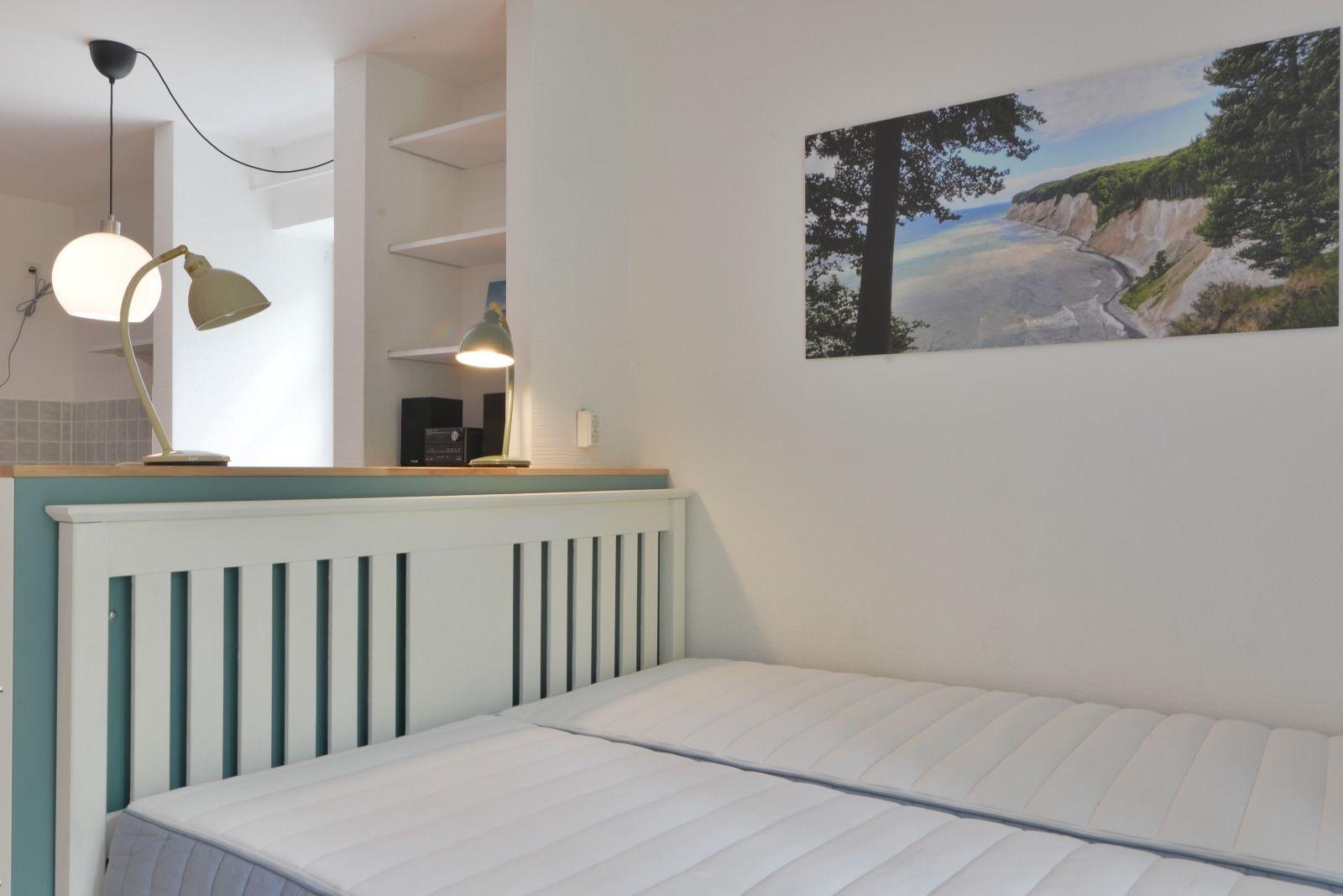 Schlafzimmer mit Bett, Wandbild und Lampe. Hintergrund zeigt Badezimmer.