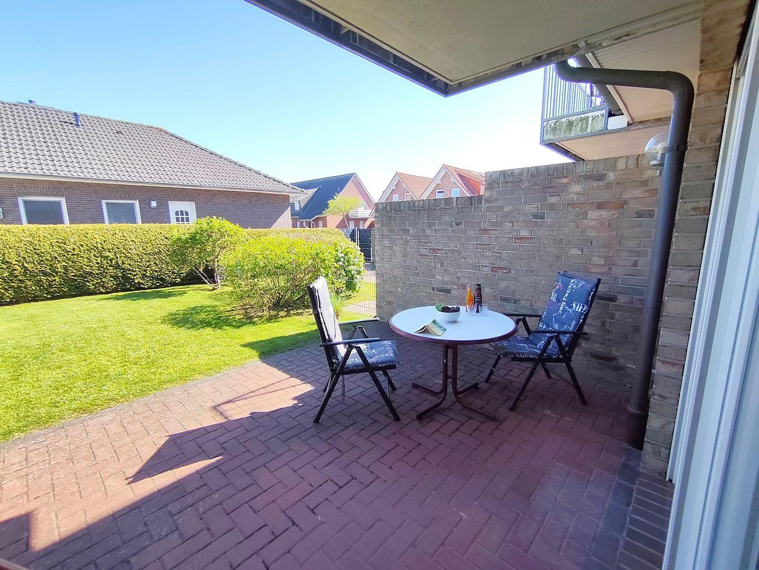 Terrasse mit Tisch und zwei Stühlen, umgeben von Garten und Mauer.