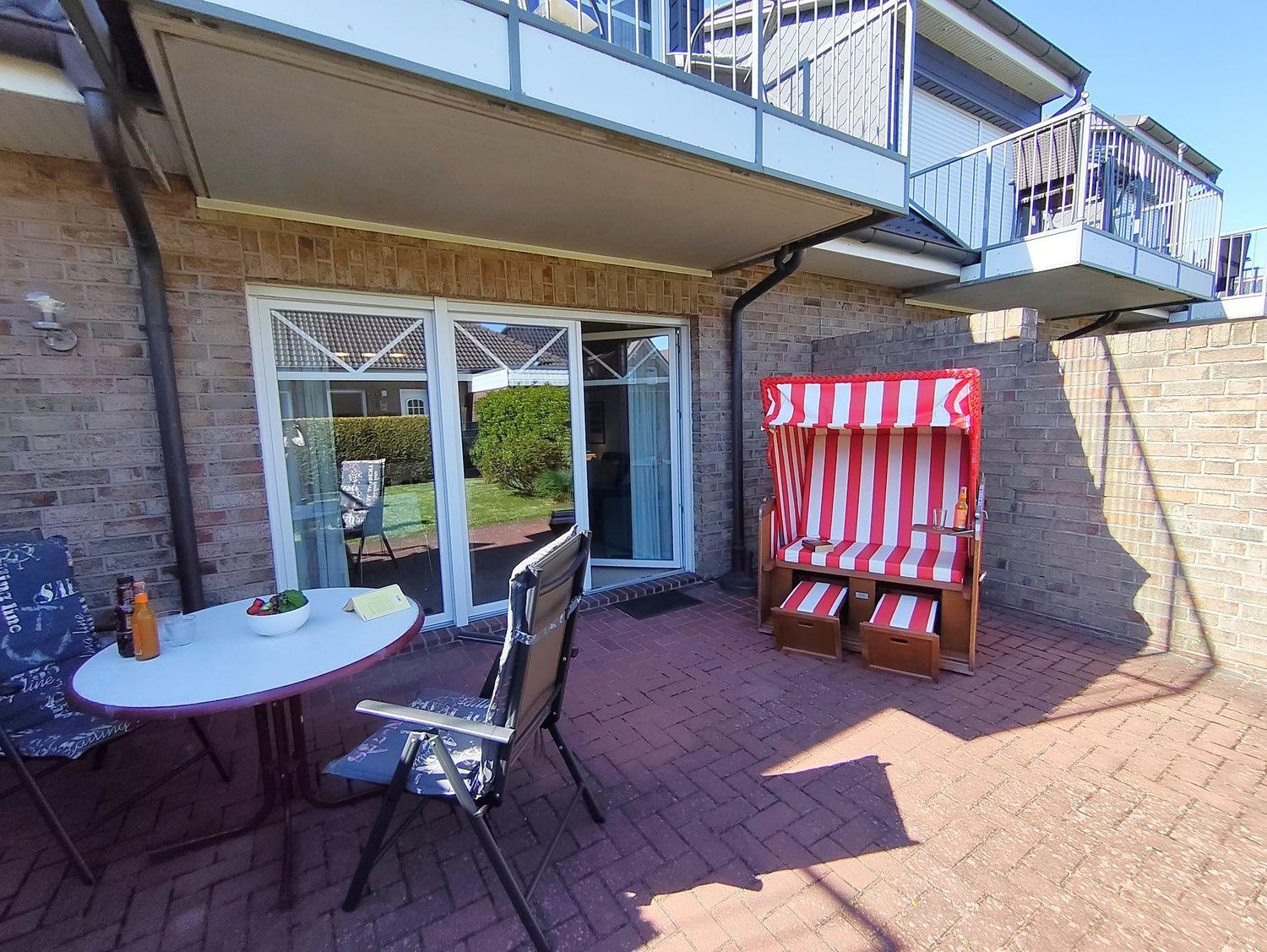 Terrasse mit Liegestuhl, Tisch und Stühlen. Hinterhof mit Glasfront und Balkon.