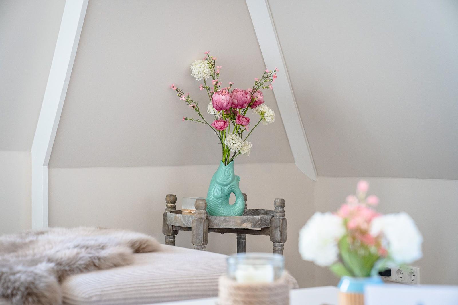 Schlafzimmer mit Blumenarrangement und Holztisch unter schrägen Deckenbalken.