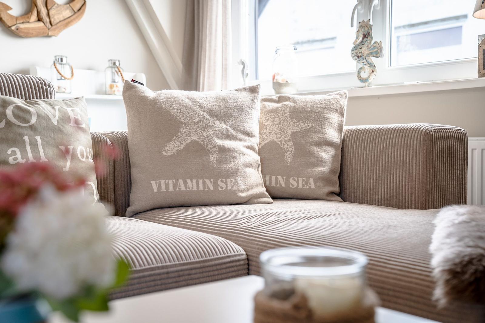 Ein Sofa mit Kissen, die Sterne und Text zeigen, vor einem Fenster mit Seepferdchen-Dekoration.