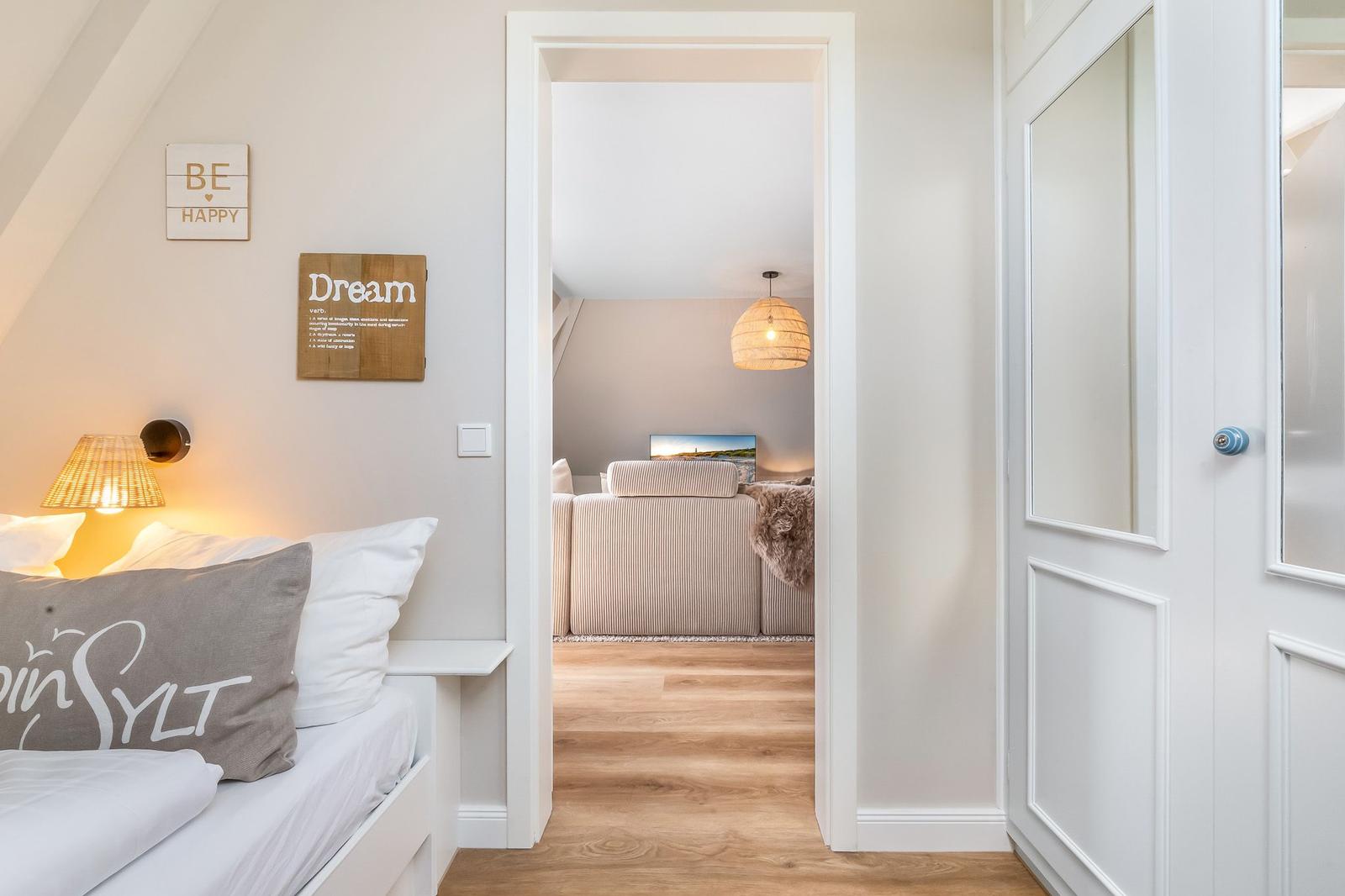 Schlafzimmer mit Blick in Wohnbereich mit Sofa und Deckenlicht.
