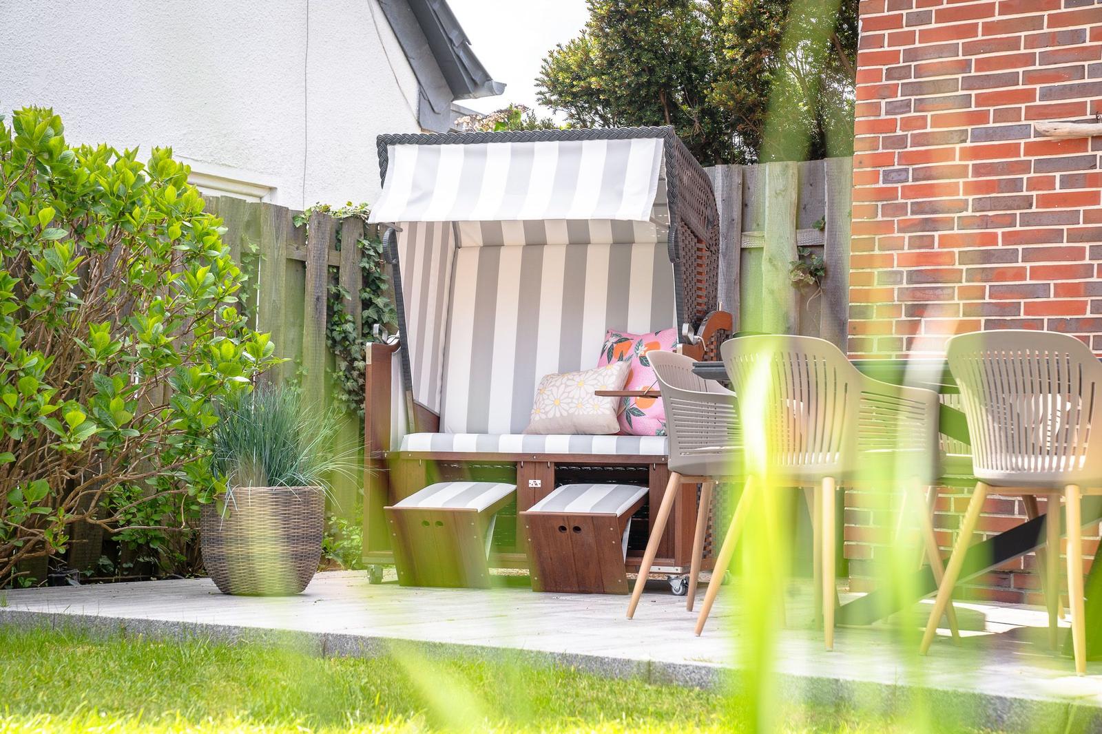 Terrasse mit Liege, Tisch und Stühlen, umgeben von Pflanzen und Mauer.