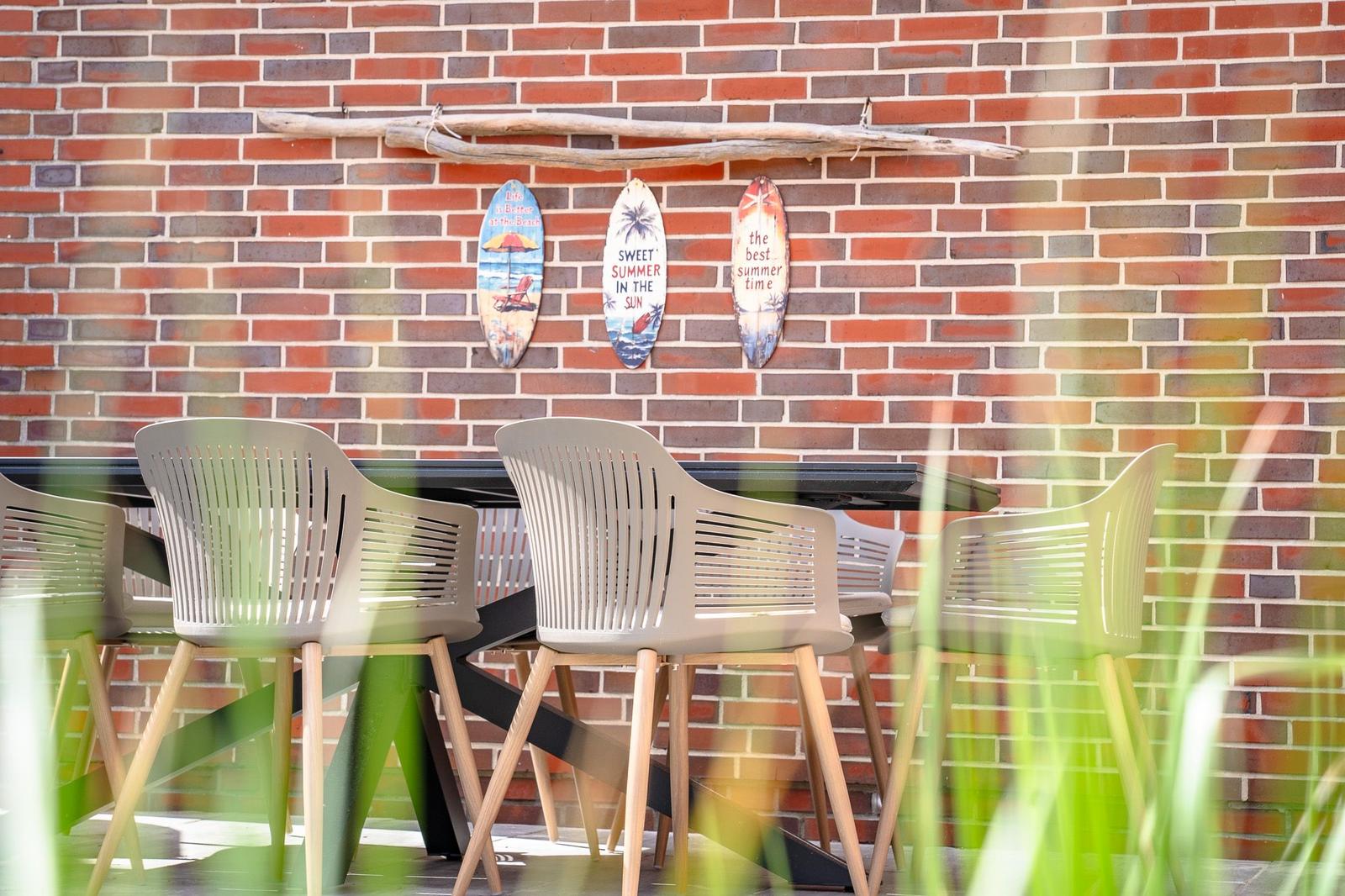 Außenbereich mit Tisch und Stühlen vor Backsteinwand mit Surfboards.