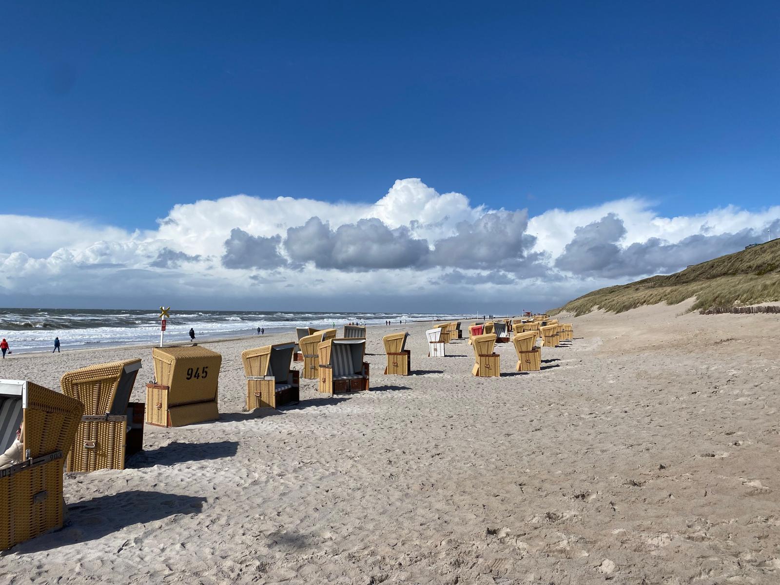 Strand mit Strandkörben und Wellen unter blauem Himmel mit Wolken.