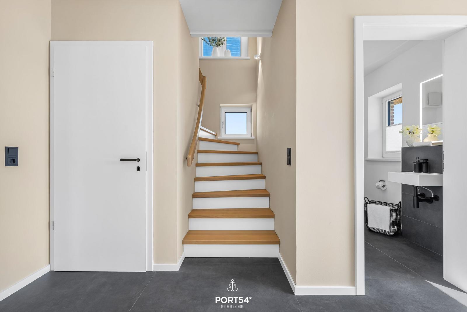 Hallway with wooden stairs, bathroom, and door