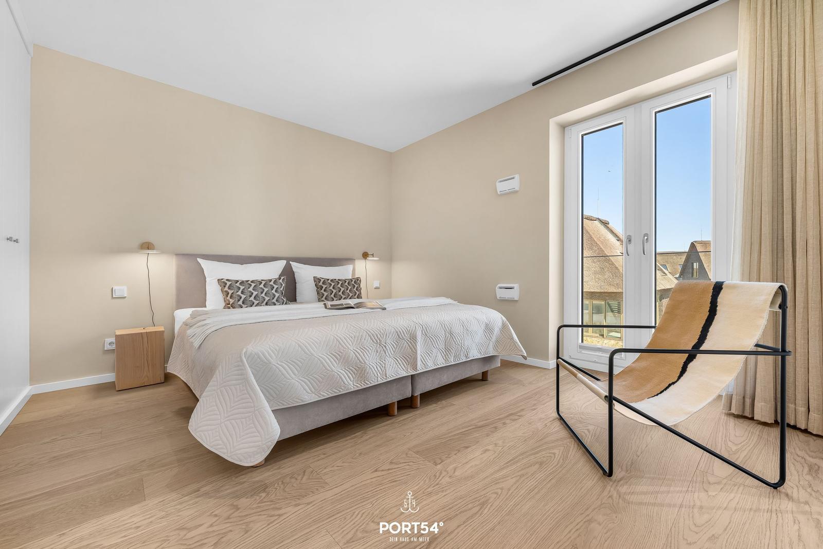 Bedroom with bed, nightstand, and chair. Window with view of rooftops.