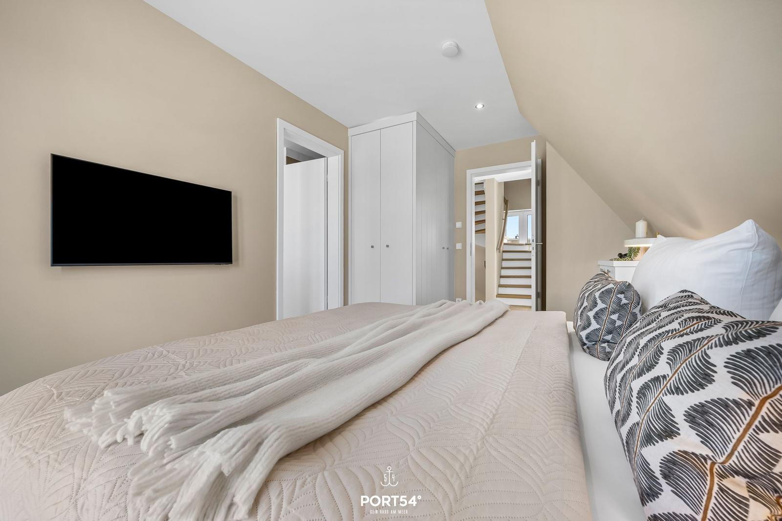 Bedroom with bed, TV, and wardrobe. Attic with staircase.