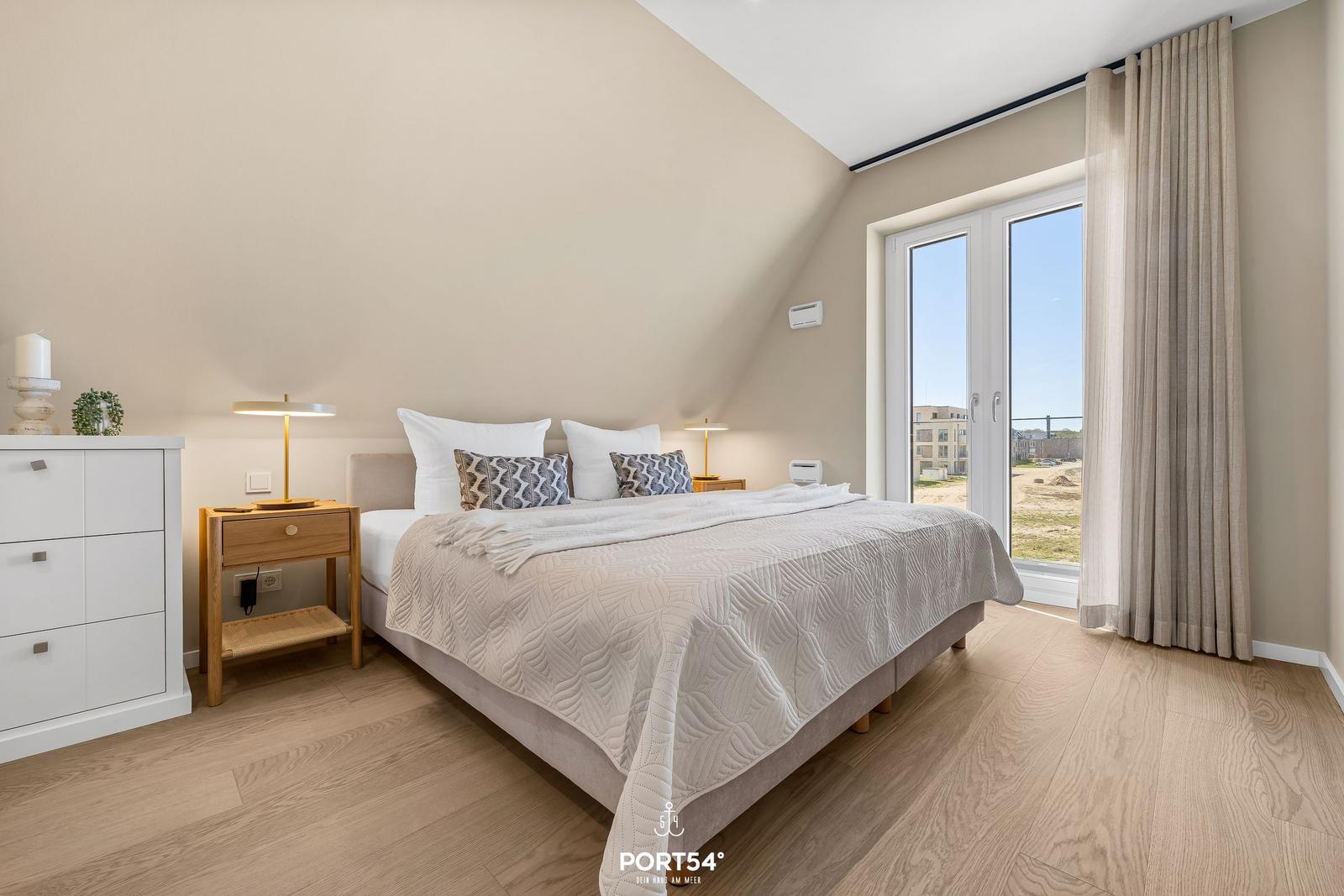 Bedroom with bed, nightstand, and window. Wooden floor and beige walls.