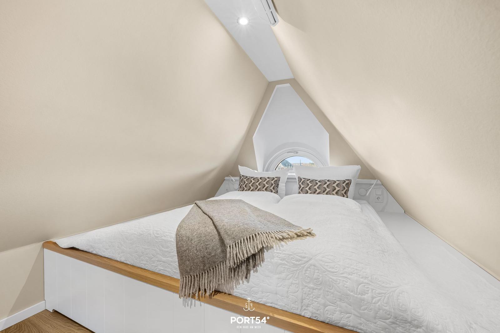 Bedroom with sloped ceiling, bed with white bedding and patterned blanket.