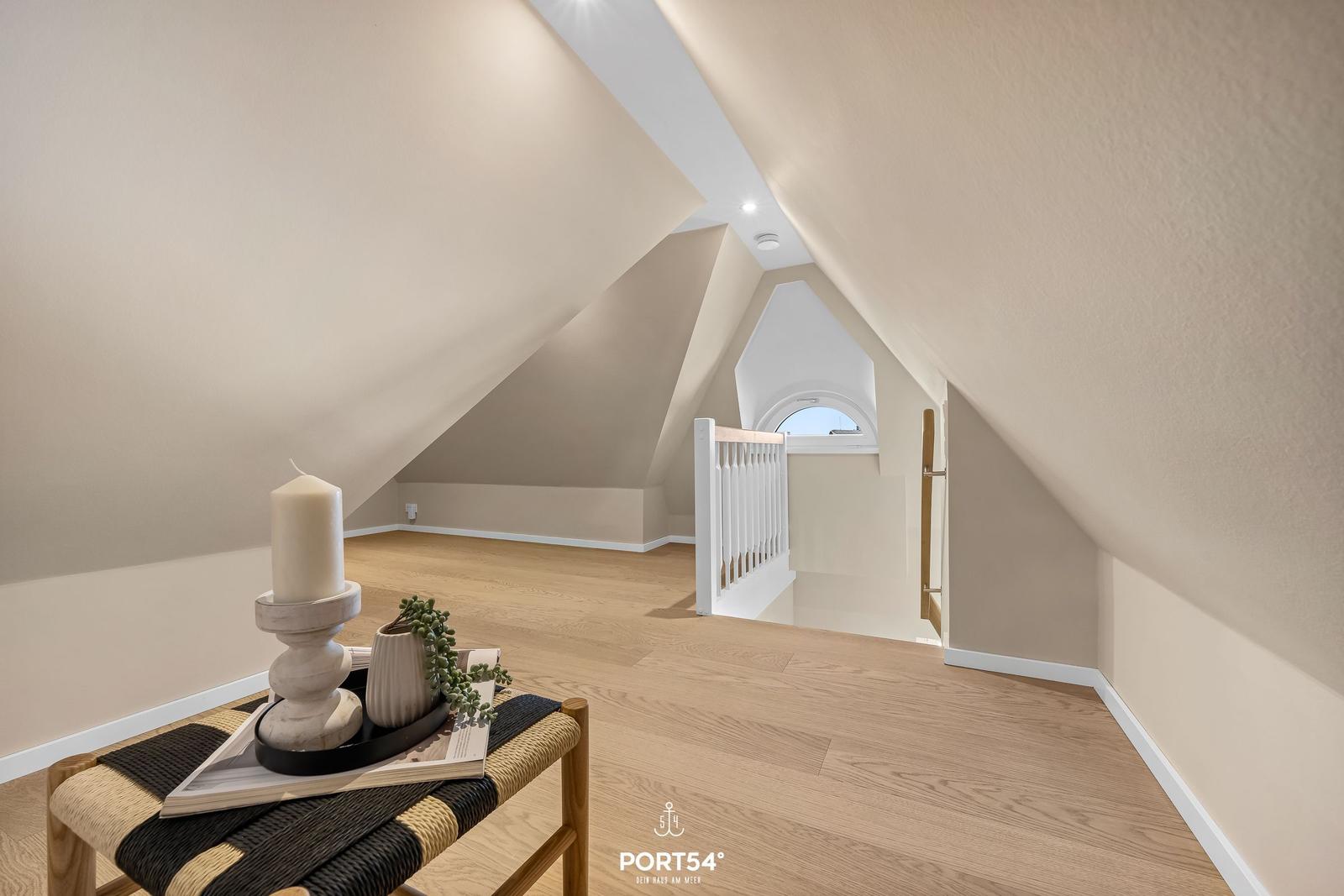 Attic with wooden floor, white walls, and a window. A small table with a candle and plant.