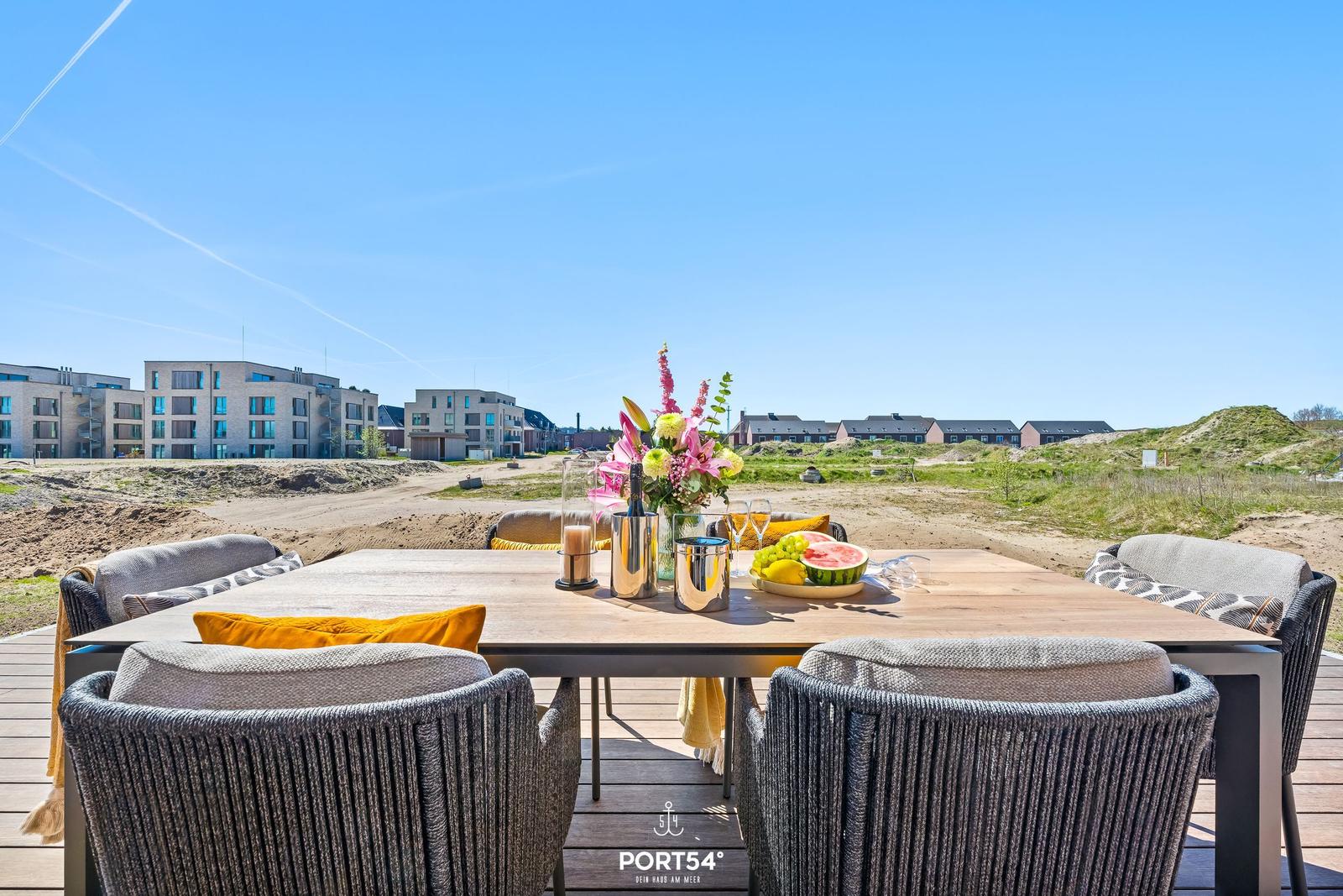 Terrace with table and chairs, view of modern buildings and dunes.