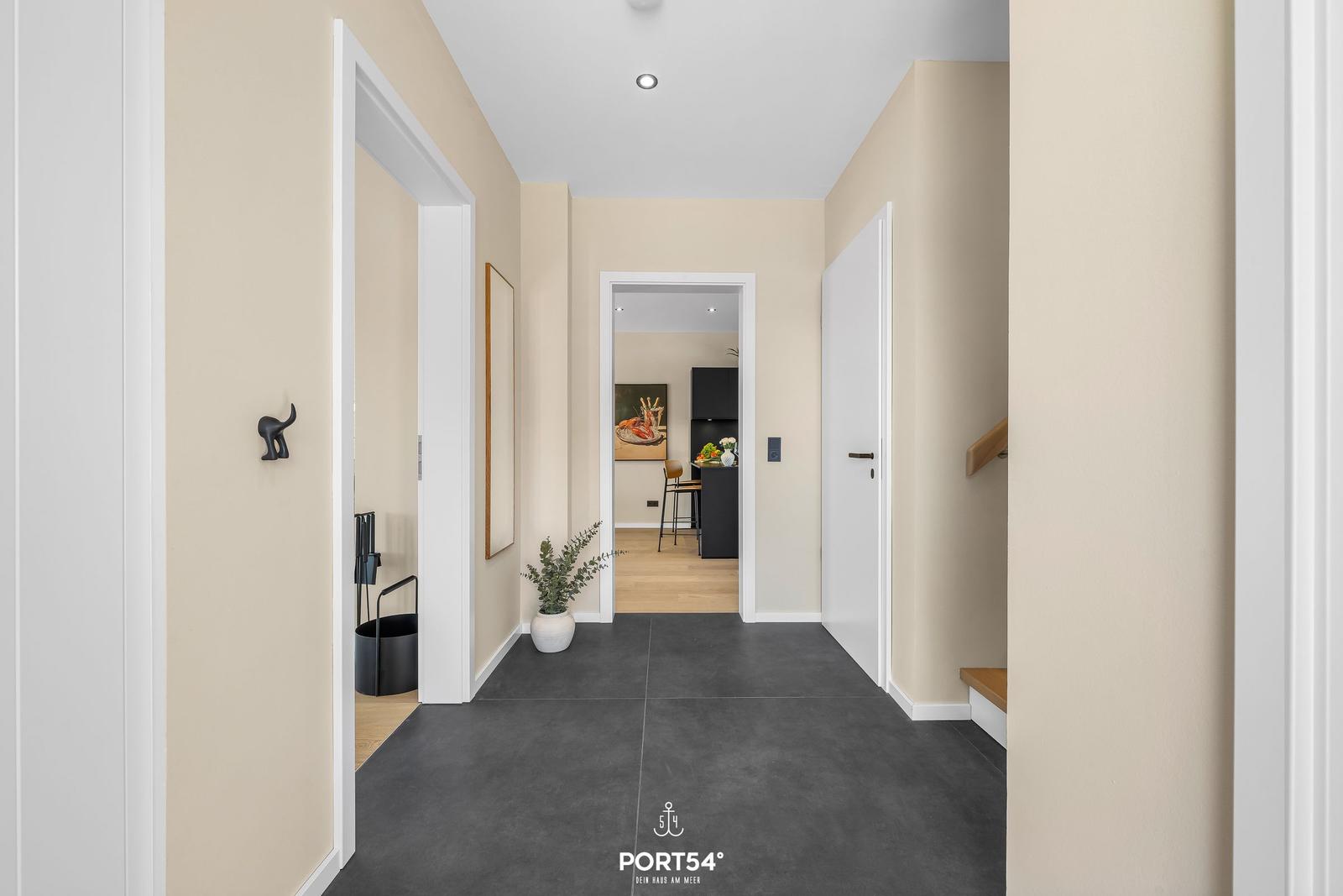 Hallway with dark floor, plant, and view into kitchen.