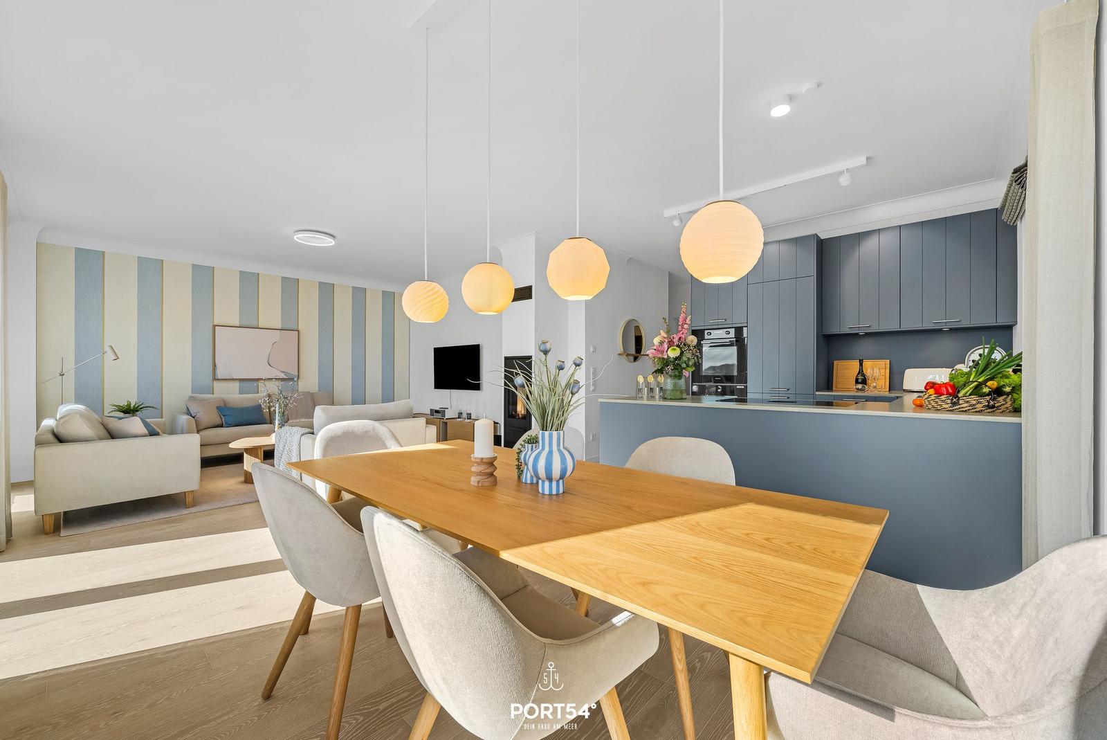 Dining area with wooden table and chairs, kitchen with blue cabinets and living room with striped wall.
